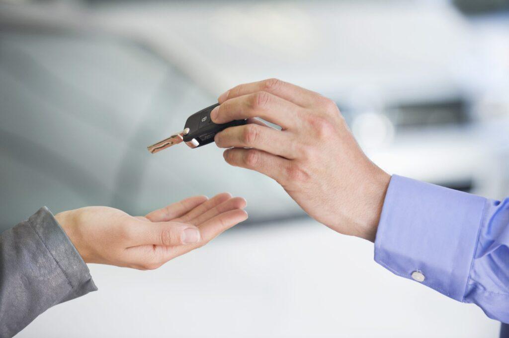 Two hands exchanging car keys; the left hand receives, while the right hand offers the keys