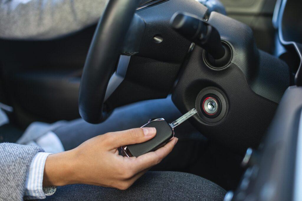 A hand holds a car key inserted into the ignition of a modern vehicle
