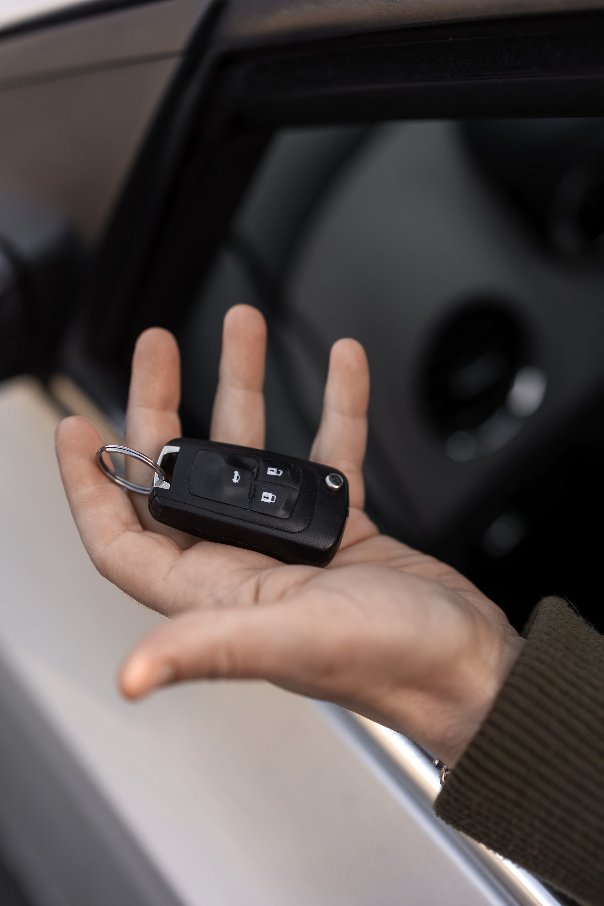 Close-up of a hand holding a black car key fob with buttons for lock and unlock